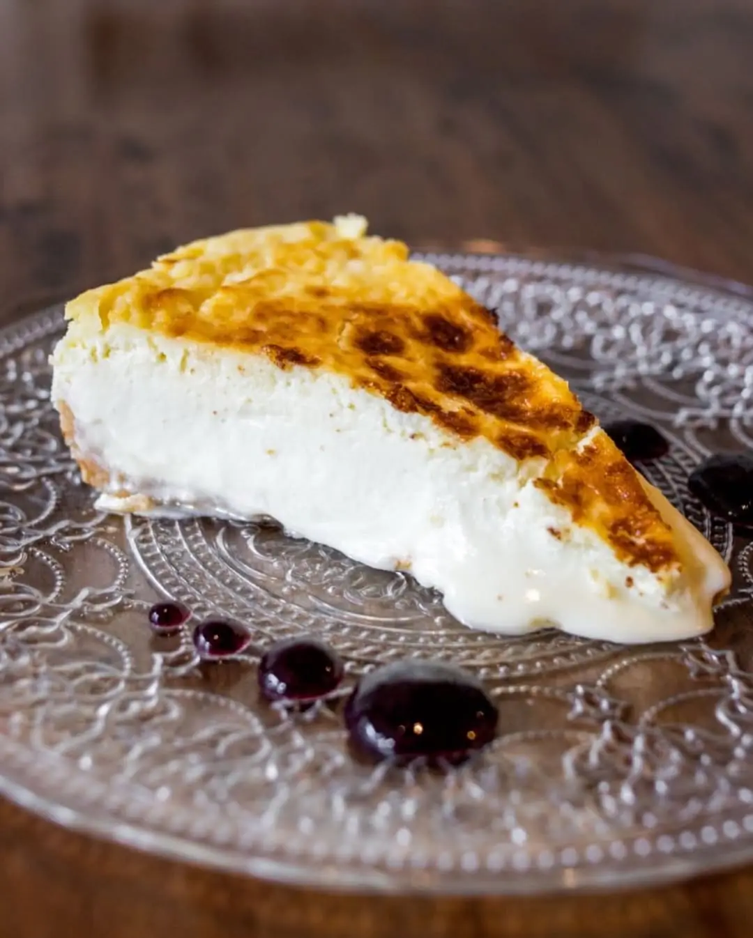 Slice of burnt Basque-style cheesecake with a blueberry compote on a decorative glass plate