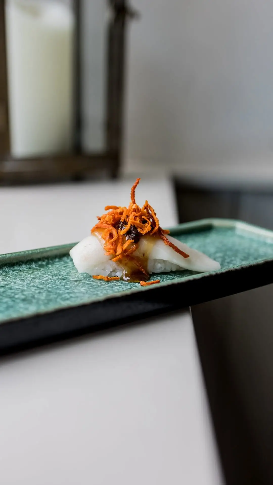 Seared white fish nigiri topped with crispy shredded vegetables and sauce on a green plate