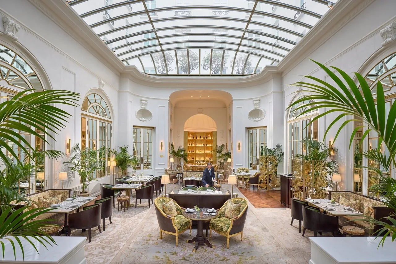A bright dining room with a glass roof, palm plants and set tables