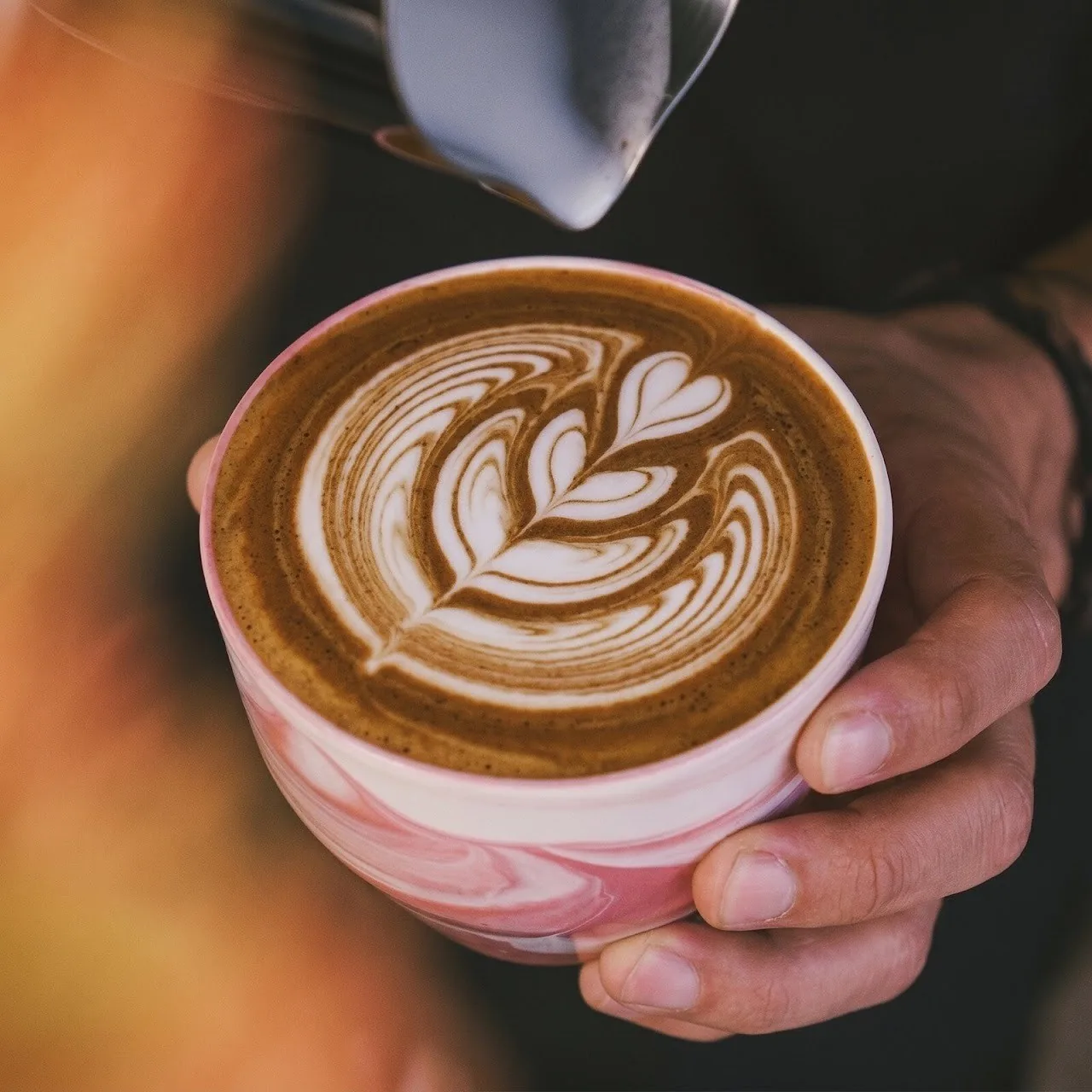A hand holding a cup of latte with a detailed leaf pattern