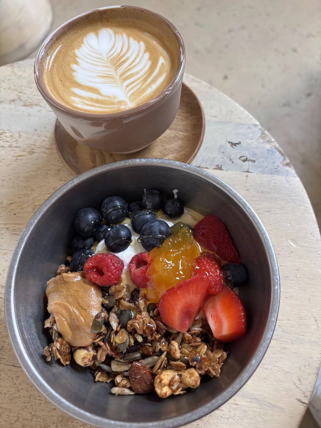 A bowl of granola with berries and jam beside a latte