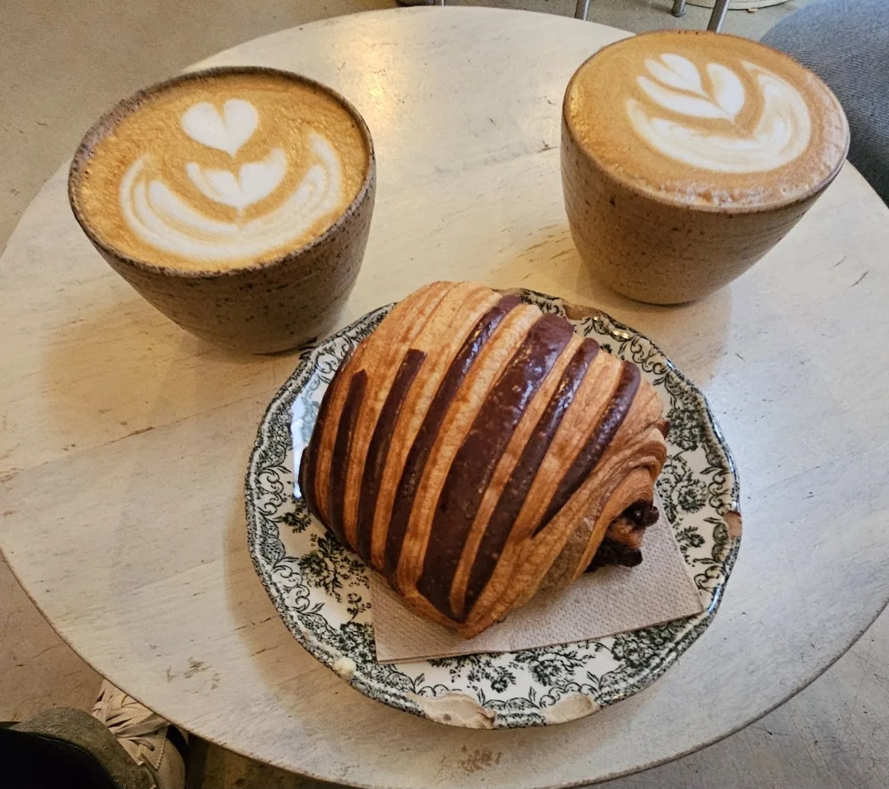 Two lattes with leaf-pattern art beside a swirled pastry