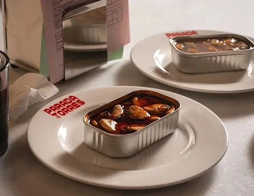 Two open tins of mussels in escabeche sauce served on white plates on a marble counter, Parada Torres
