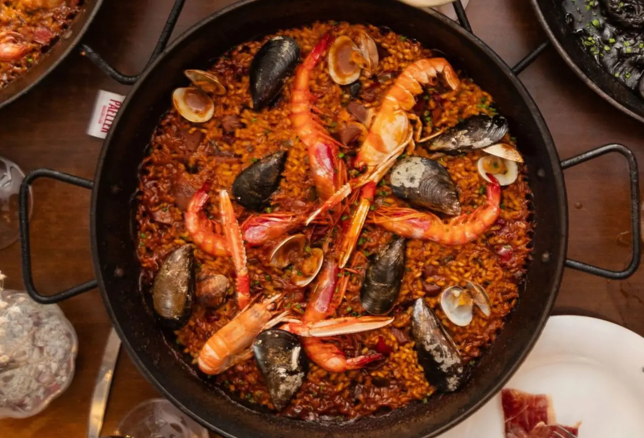 Seafood paella in a black pan topped with mussels, clams and whole prawns, served on a wooden table at Pasa Tapas