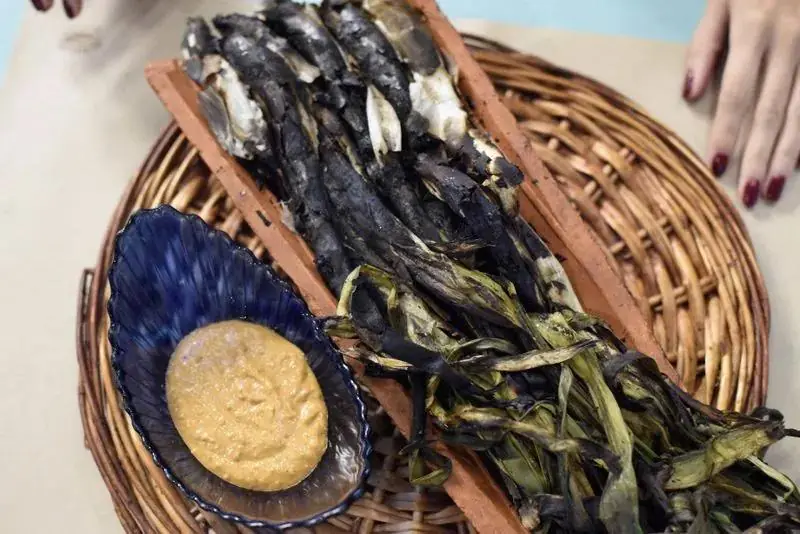 Grilled calçots on a wooden board with a bowl of romesco-style dipping sauce at Pasa Tapas