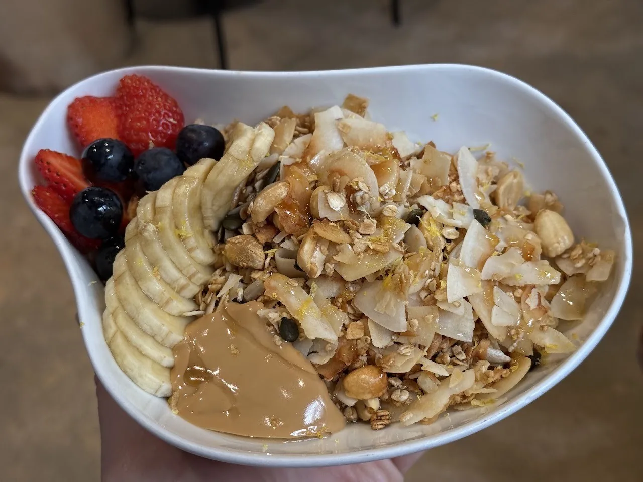 A bowl of granola with banana slices, berries and nut butter