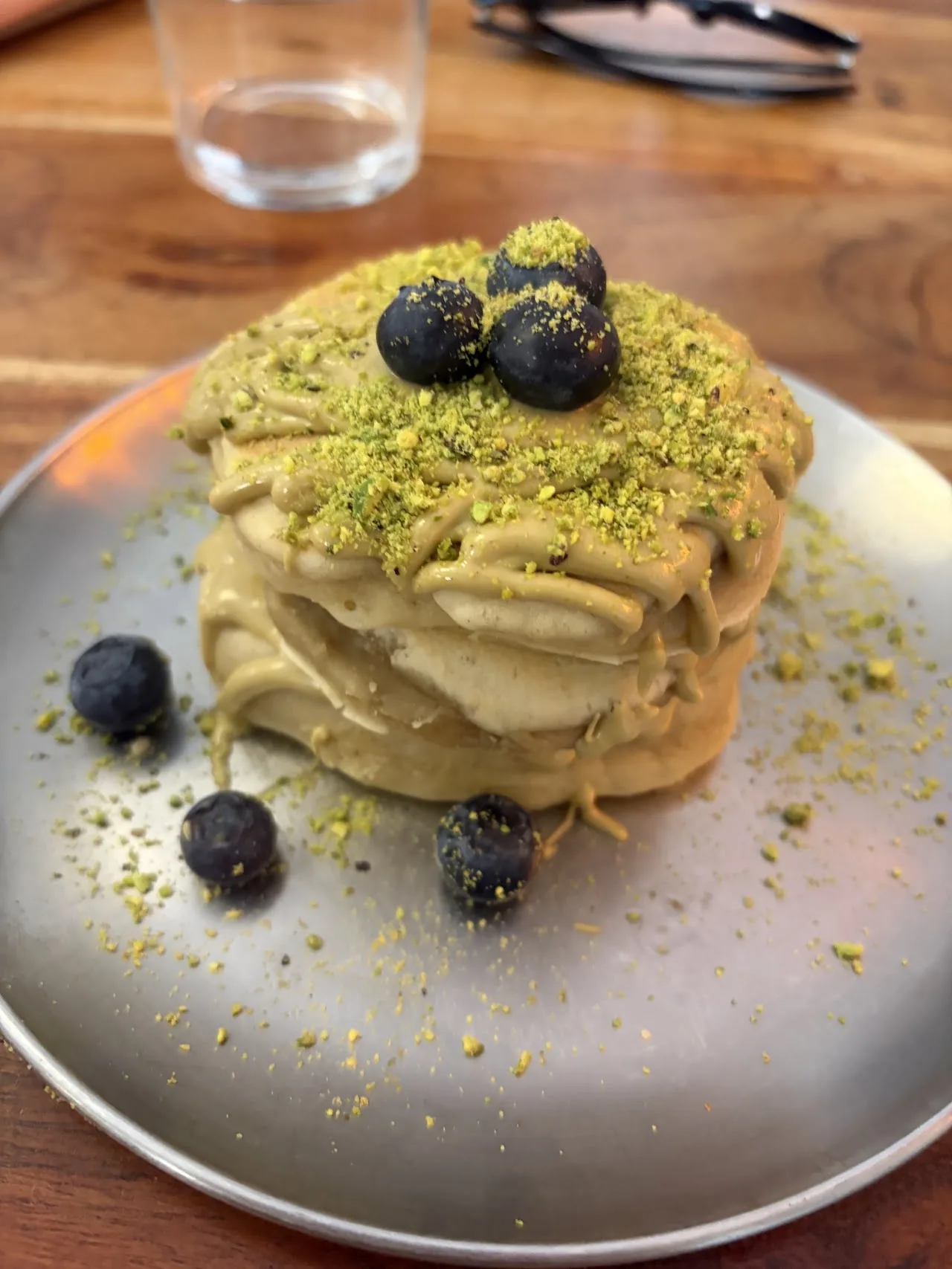 A layered pistachio dessert topped with blueberries and pistachio crumble