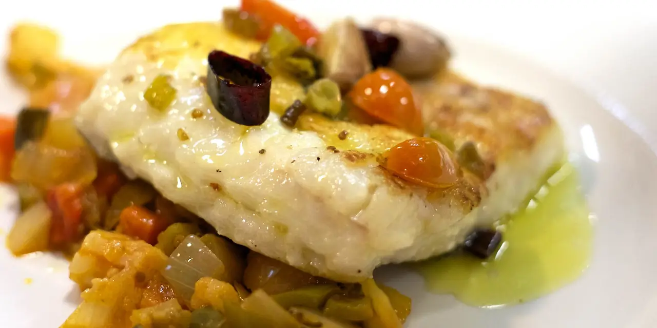 Pan-seared white fish fillet over a diced vegetable sofrito with cherry tomatoes and olives in olive oil at El Passadís del Pep