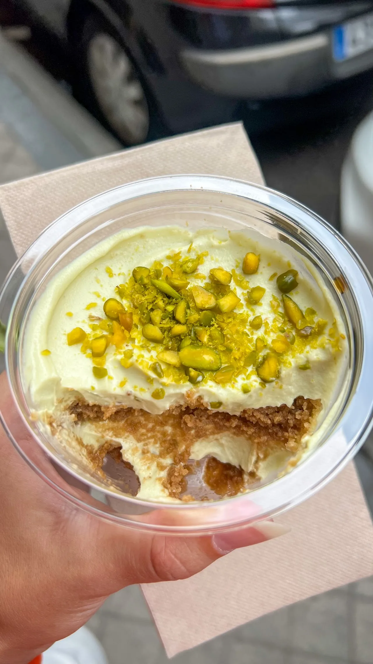 A cup of tiramisu-style dessert topped with pistachio crumbs