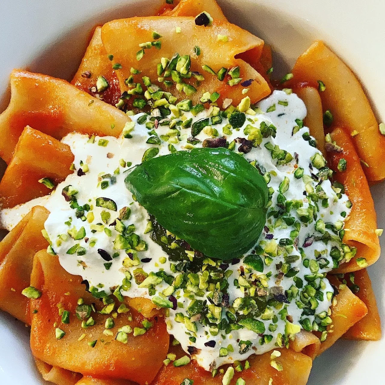 Bowl of pappardelle pasta topped with burrata, pistachios and basil