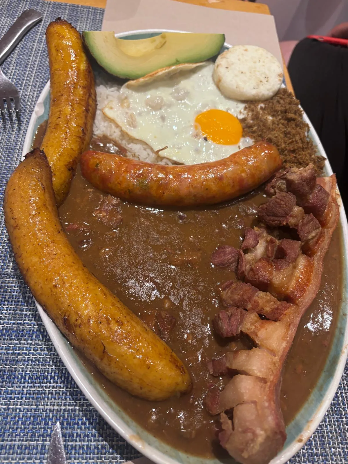 Platter of fried plantains, sausage, fried egg, avocado and a meat stew