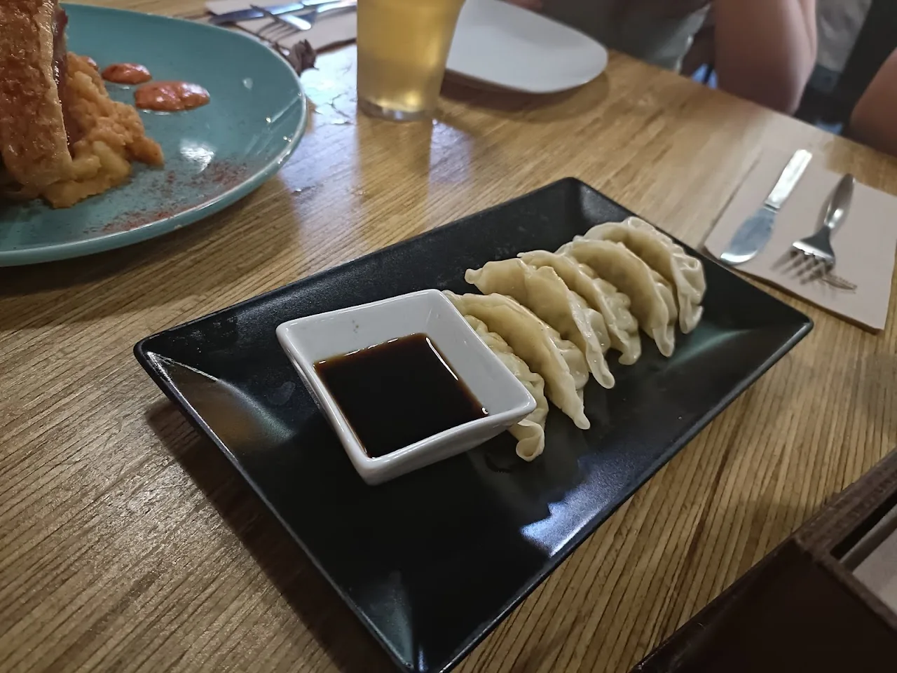 A plate of fried dumplings served with a small dish of dark dipping sauce