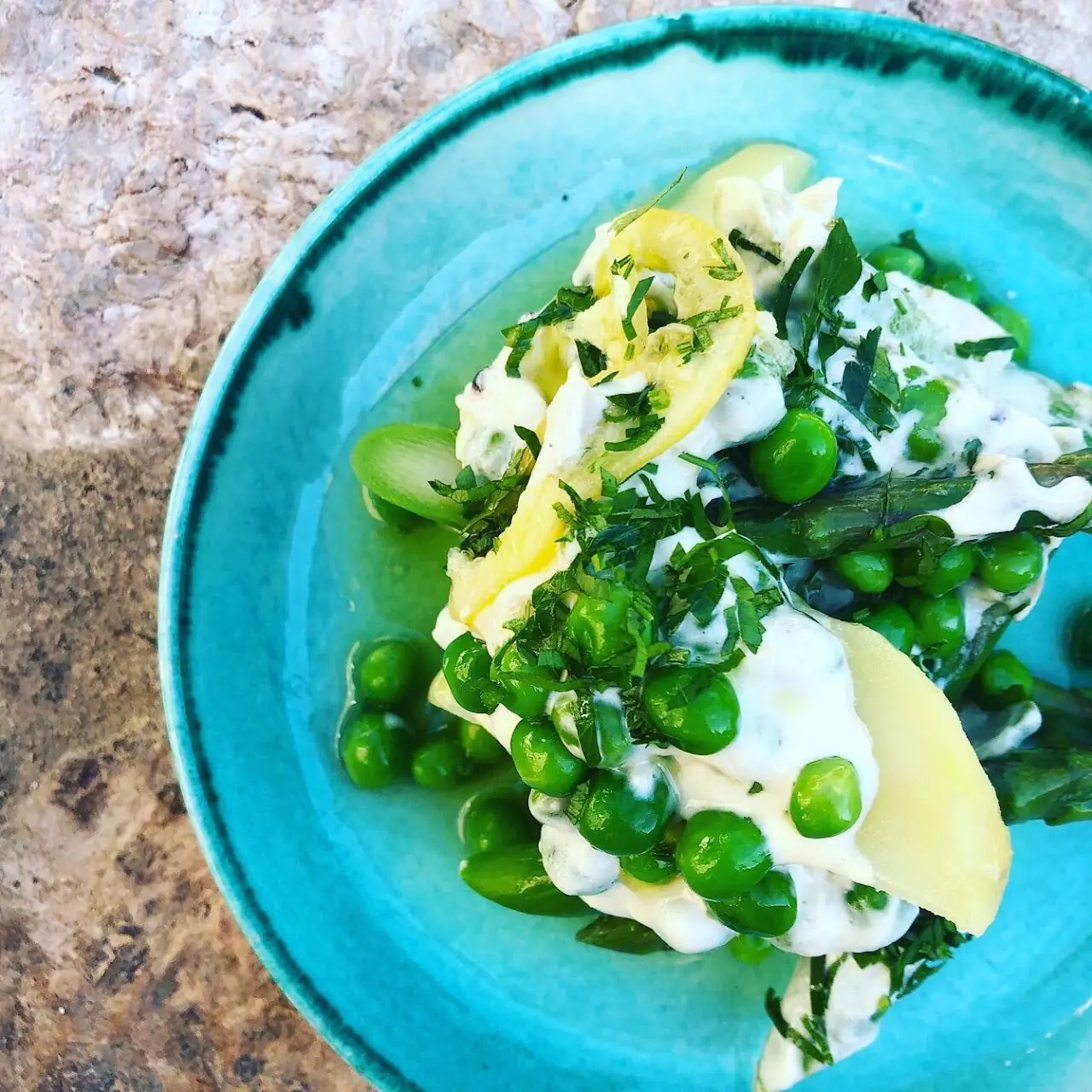 A salad of green peas, herbs, and burrata on a blue ceramic plate.