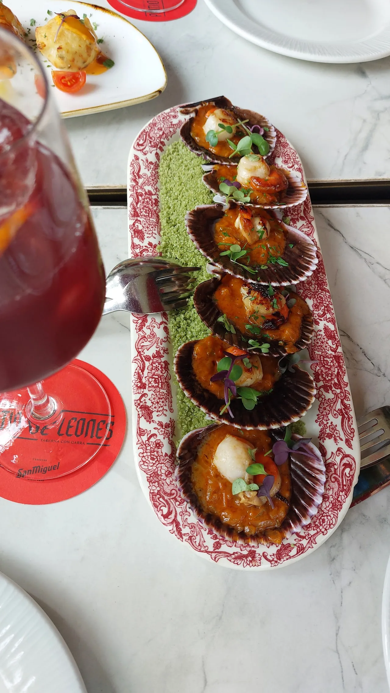 Scallop shells filled with food served on a plate alongside a red drink