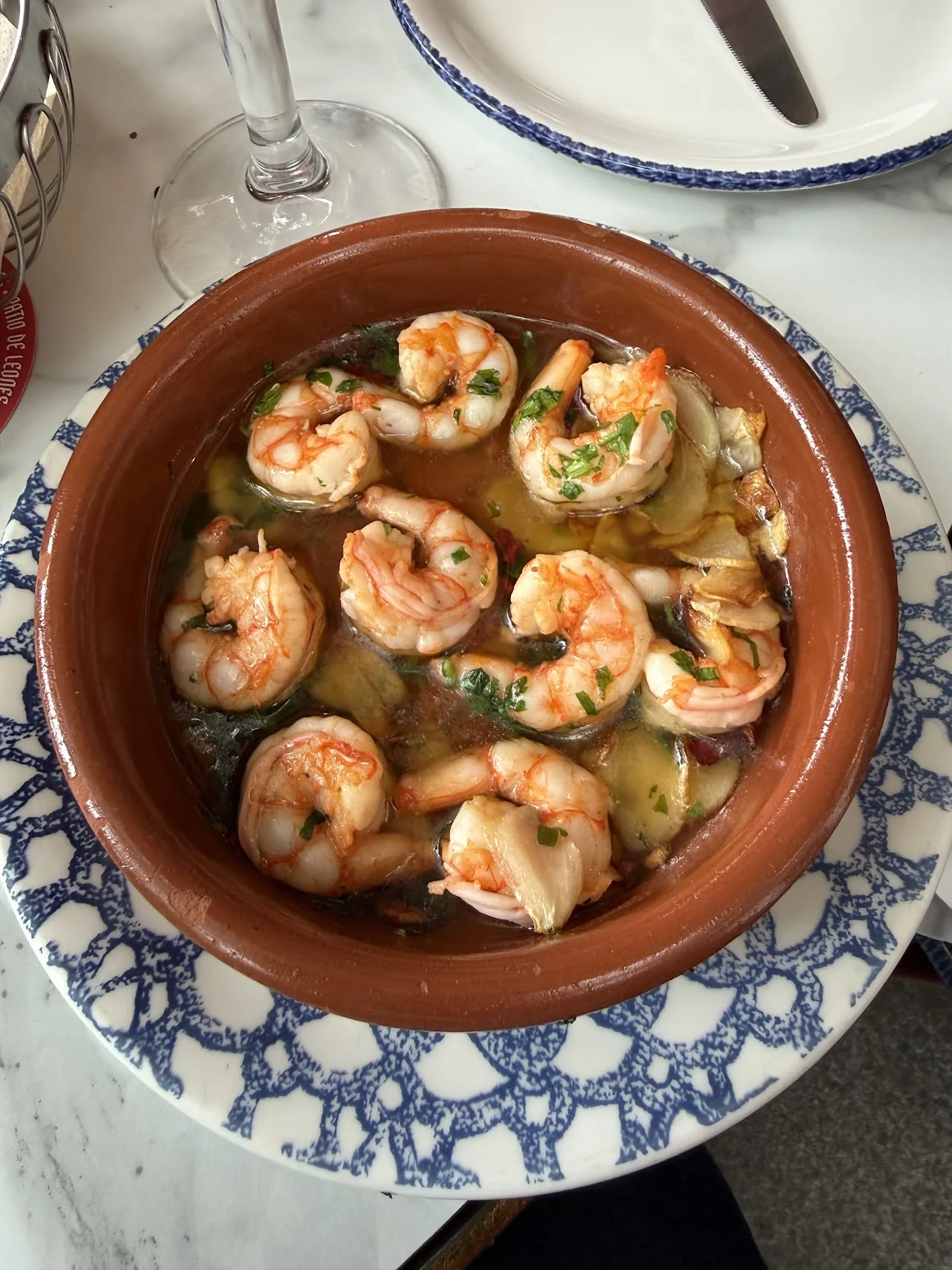 A terracotta dish of garlic shrimp with green herbs