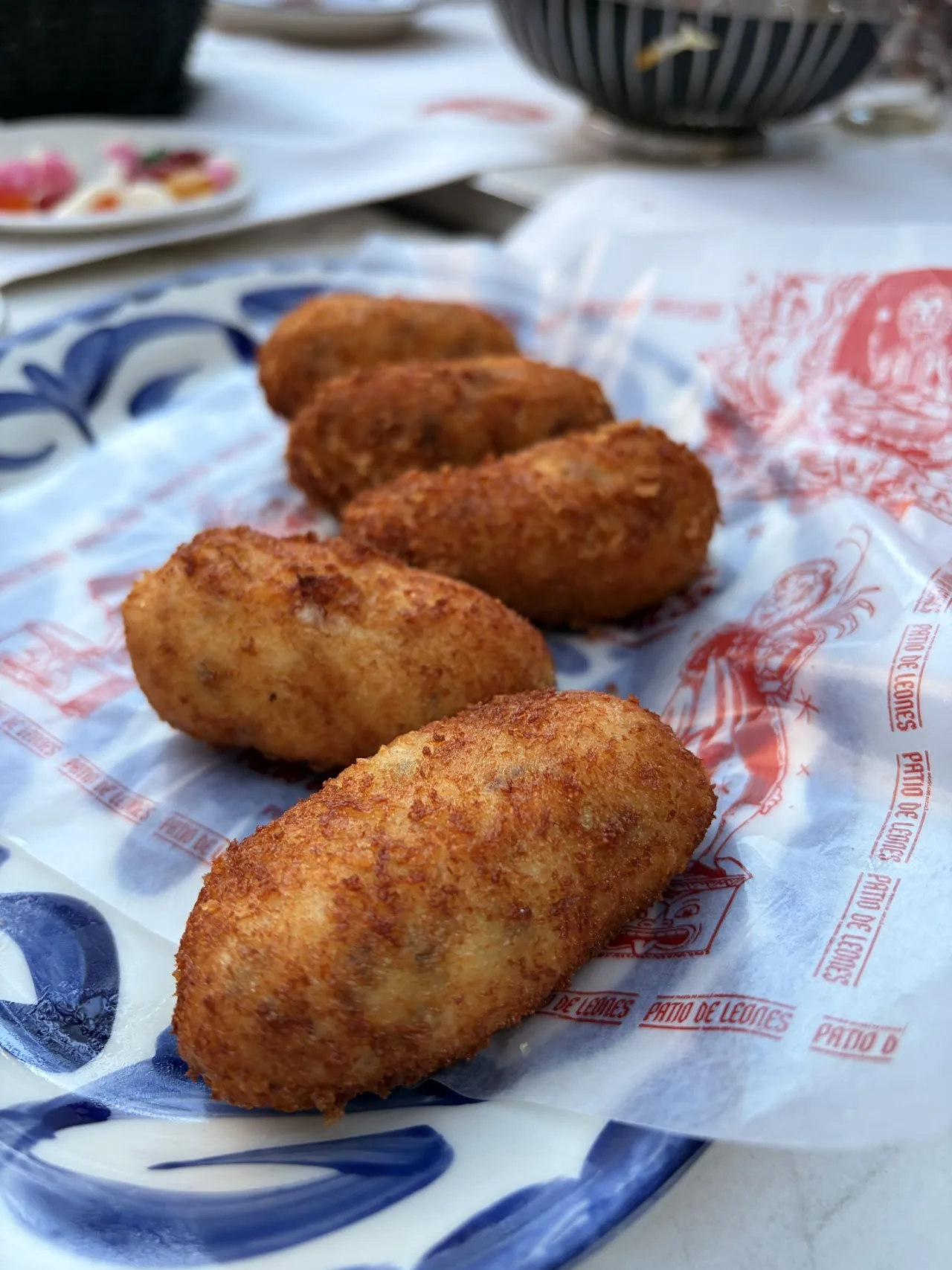 A plate of five breaded croquettes wrapped in patterned paper