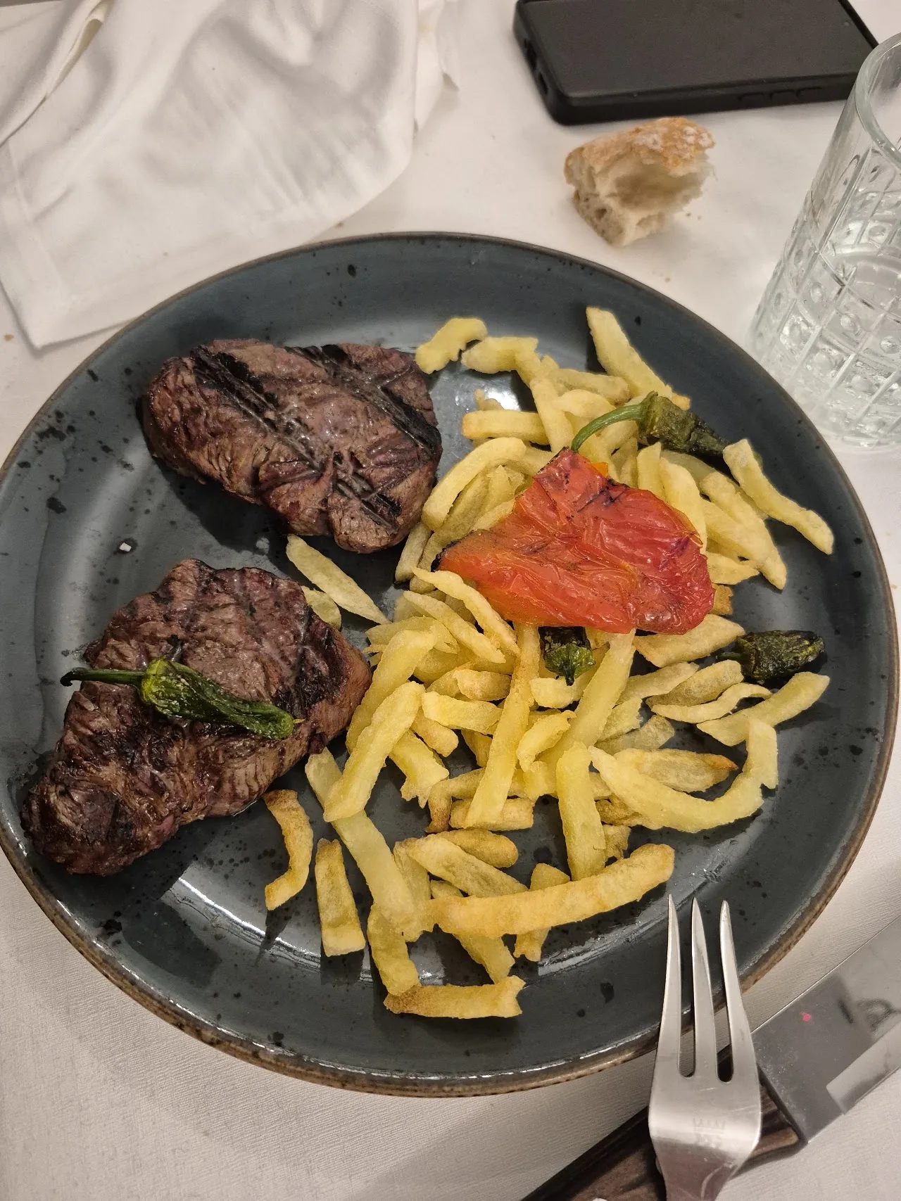 A grilled steak with fries and a slice of tomato