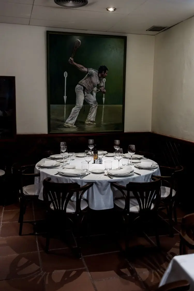Dining room corner with a set round table and bentwood chairs beneath a large green painting of a Basque pelota player