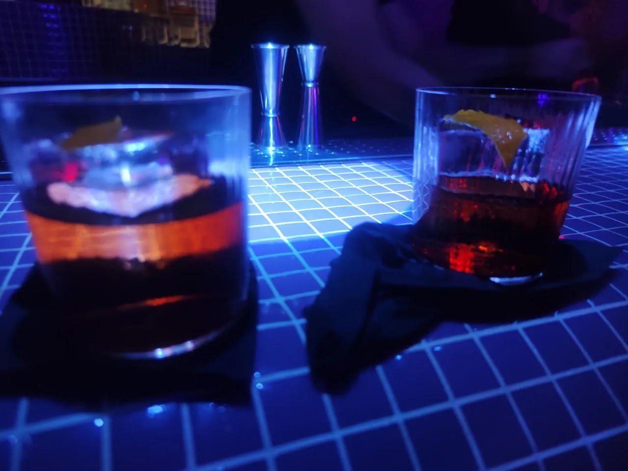 Two dark cocktails served on an illuminated blue table