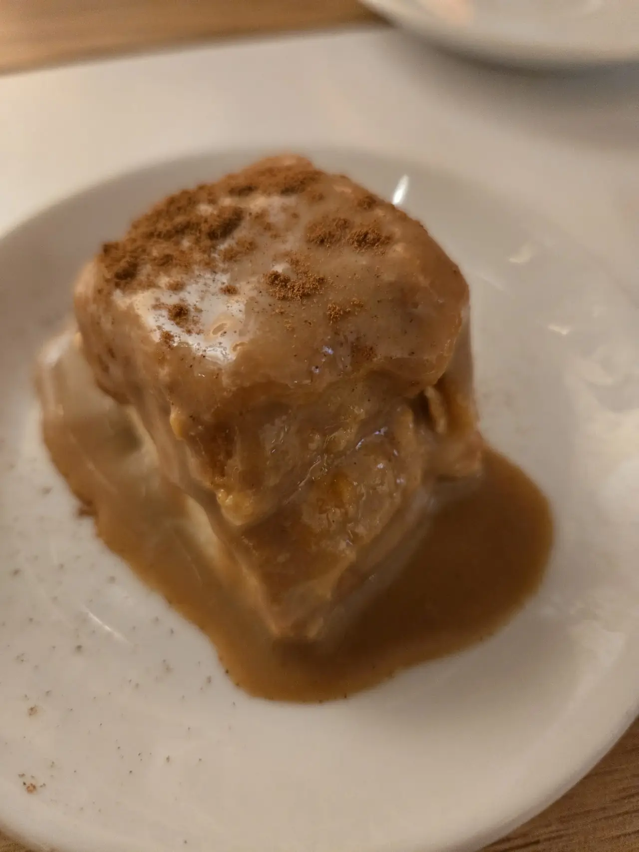 A square of bread pudding-style dessert topped with caramel sauce on a white plate