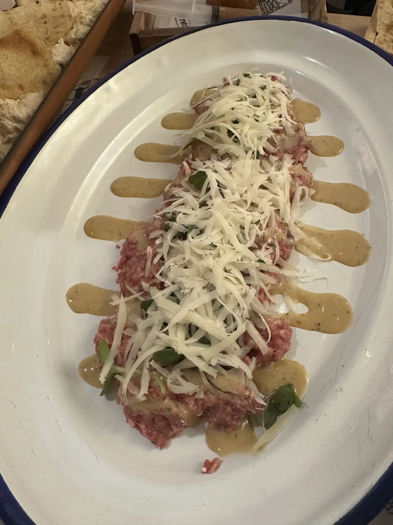 Beef tartare topped with shredded cheese and drizzled sauce on an oval plate