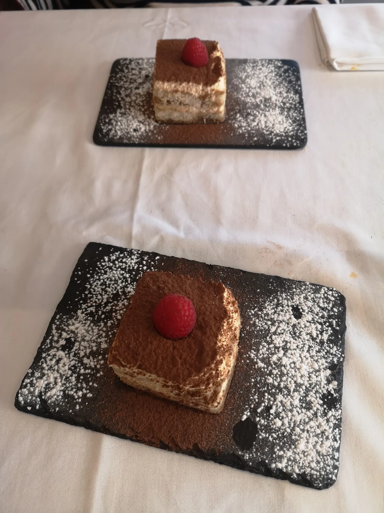 Two slices of tiramisu dusted with cocoa powder on a slate board