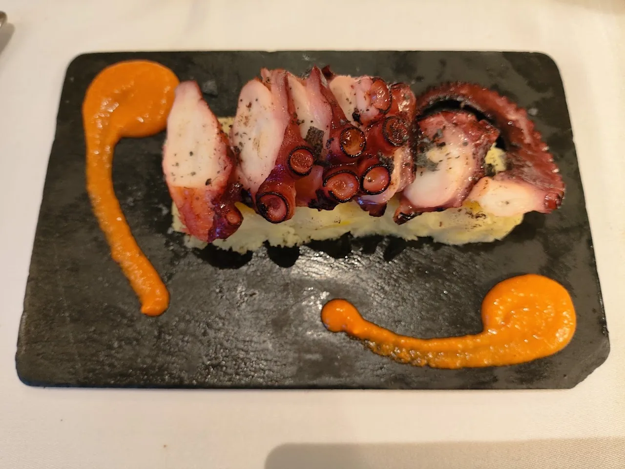 Sliced octopus arranged on a board with orange sauce