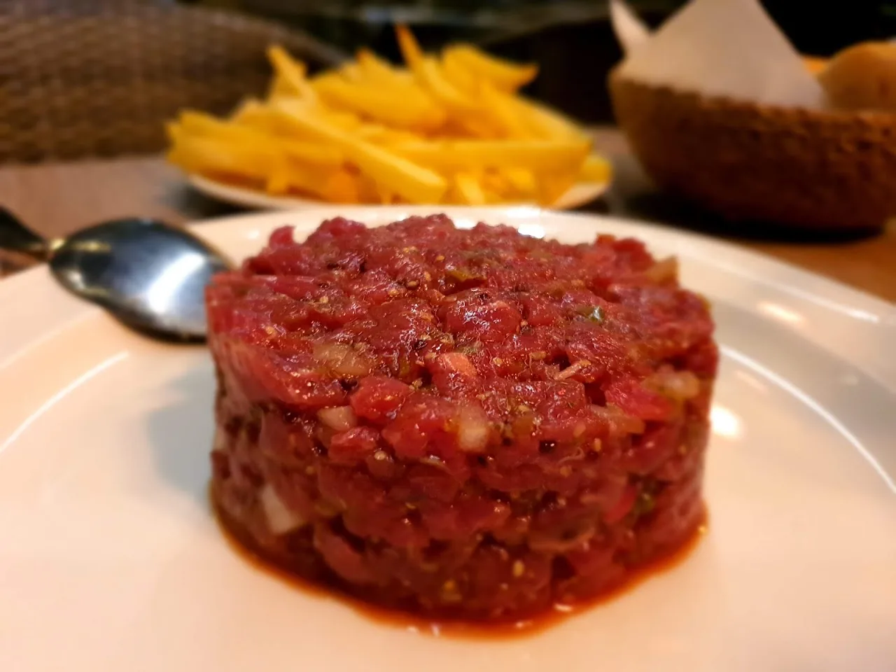 A round of steak tartare served with a side of fries