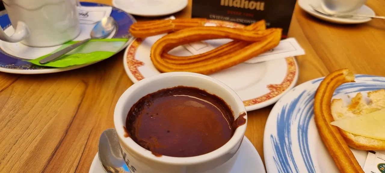 A cup of thick chocolate beside plates of churros on a wooden table