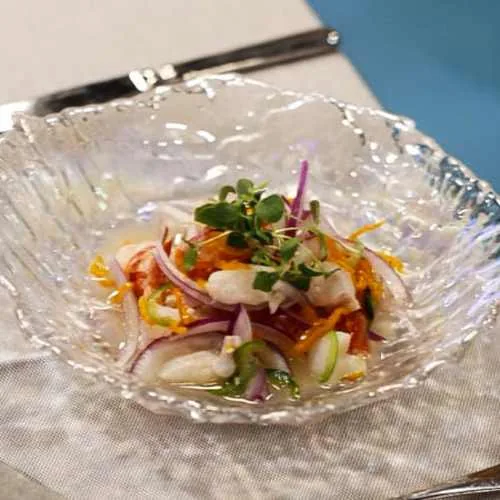 A small glass bowl of ceviche with red onion and herbs