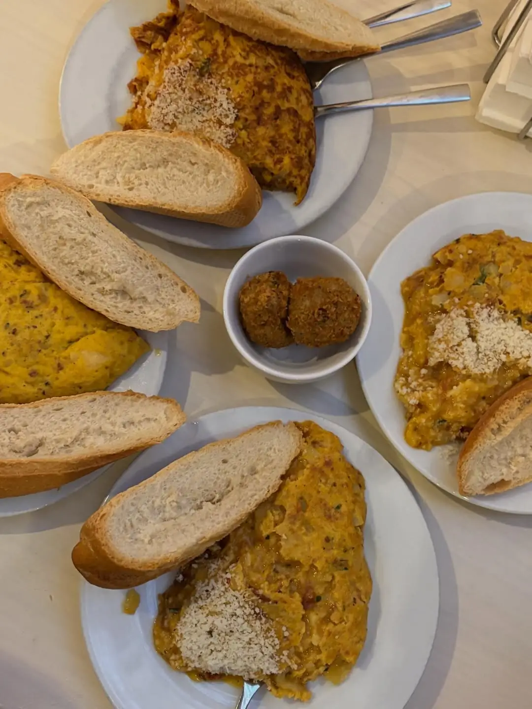 Several tortilla portions with grated cheese, croquetas and bread on plates