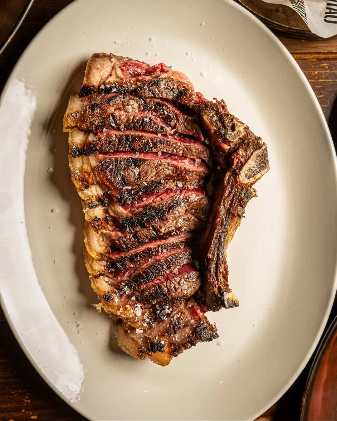 Sliced grilled T-bone steak with charred grill marks and salt crystals on a plate