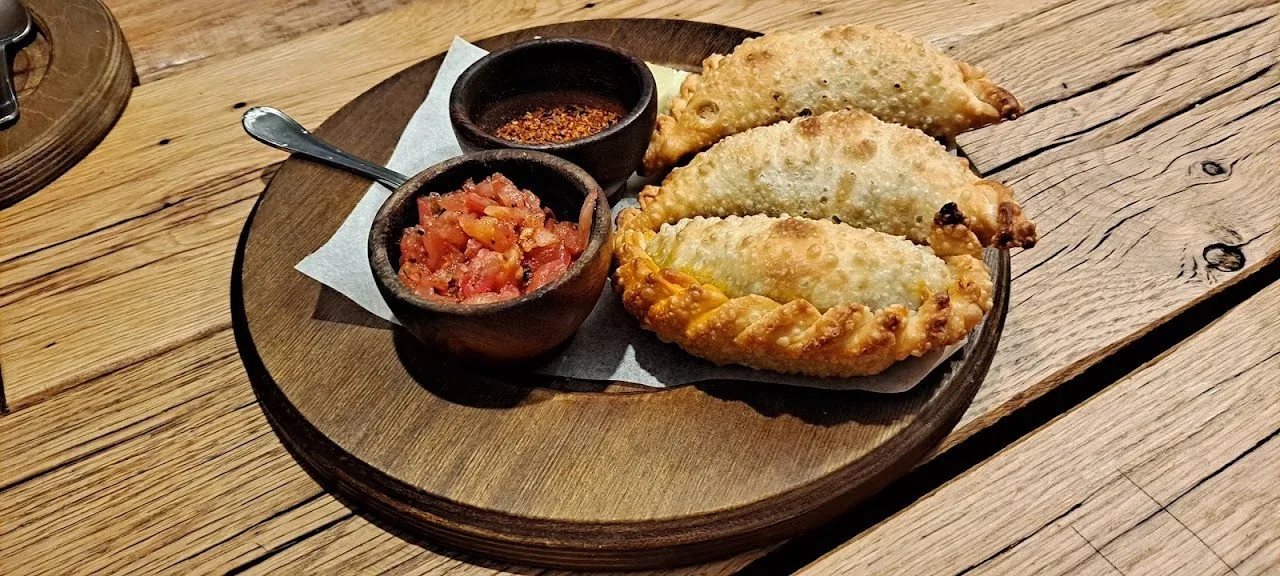 Empanadas and a small dish of salsa on a round wooden board