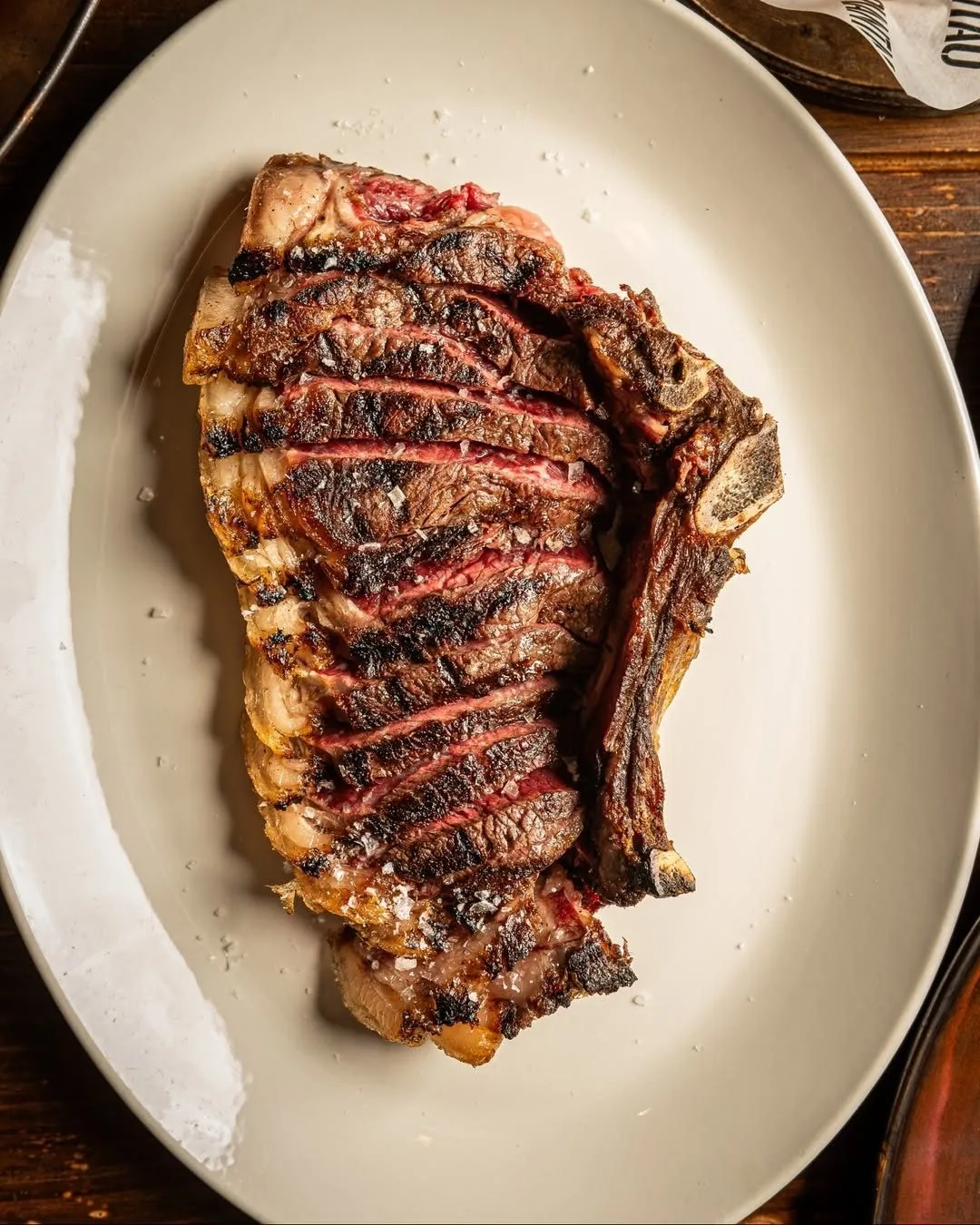 A grilled bone-in steak on a large oval white plate