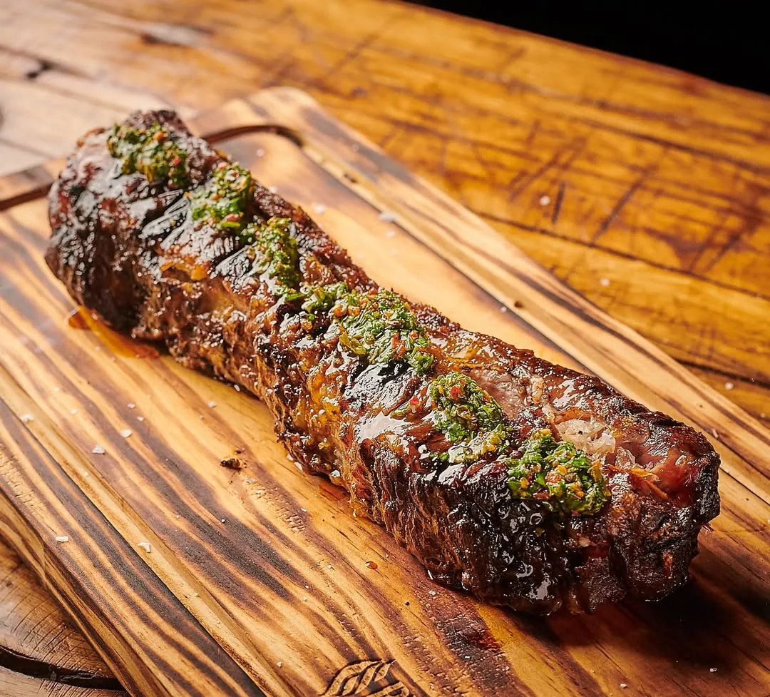 A long grilled steak fillet on a wooden board, garnished with herbs