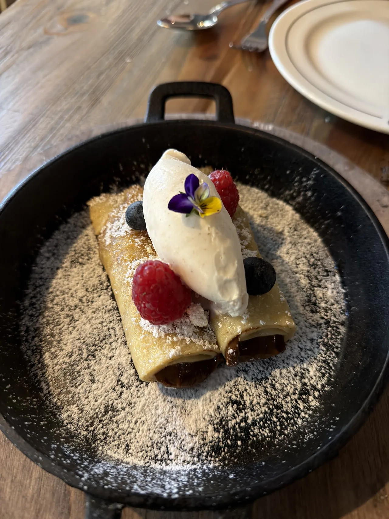A rolled crepe dessert with whipped cream and raspberries in a skillet