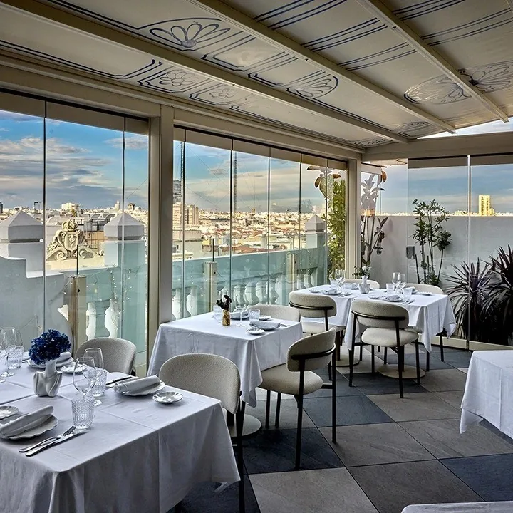 Tables set with white tablecloths beside floor-to-ceiling windows overlooking the city