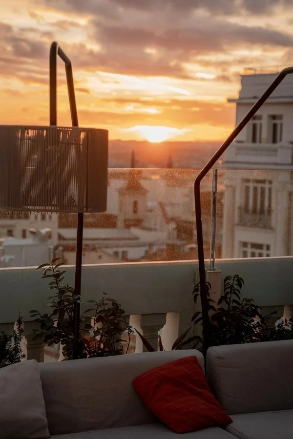 A lounge sofa with a red cushion on a terrace with a sunset sky behind