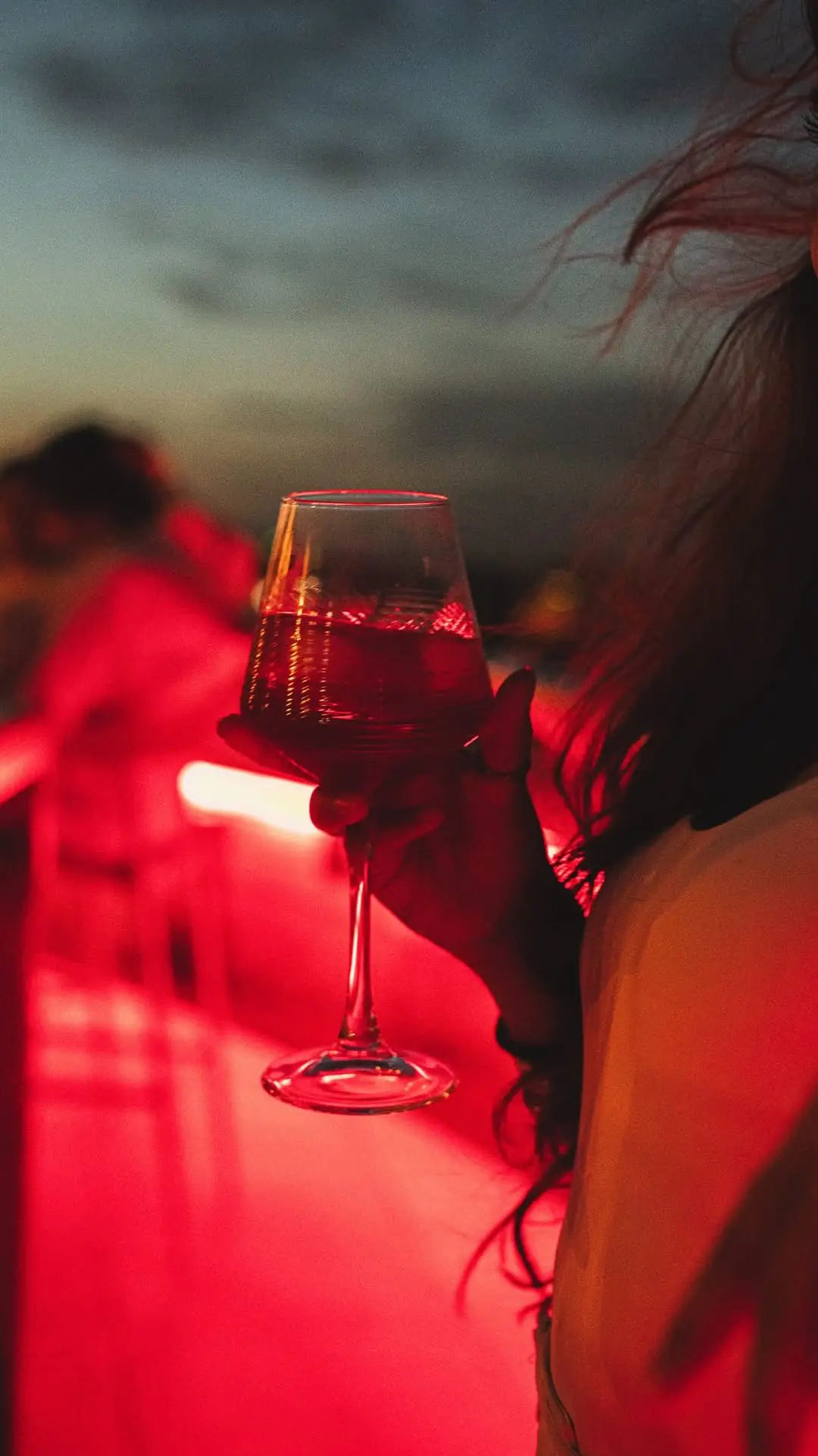 Hand holding a glass of red wine at a rooftop bar at sunset