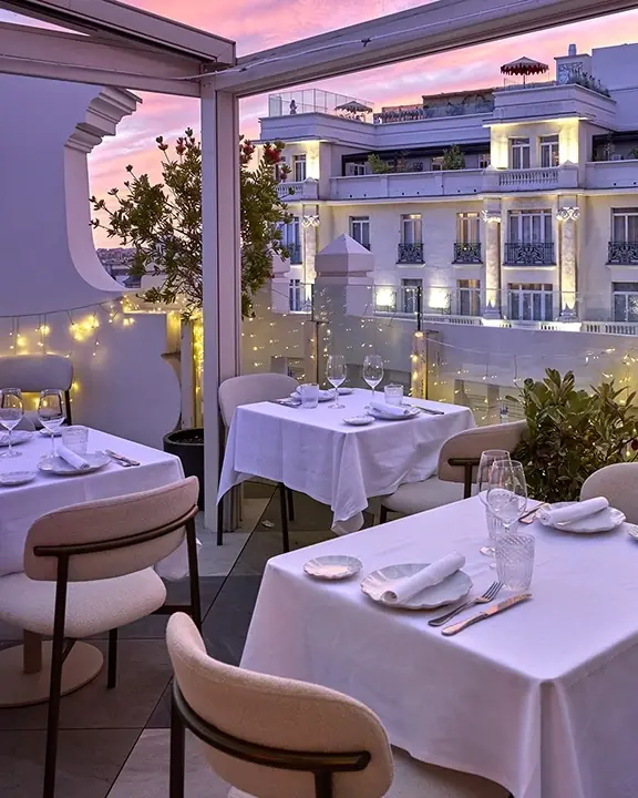 Rooftop terrace dining room with white tablecloths, glass railings, and city skyline view