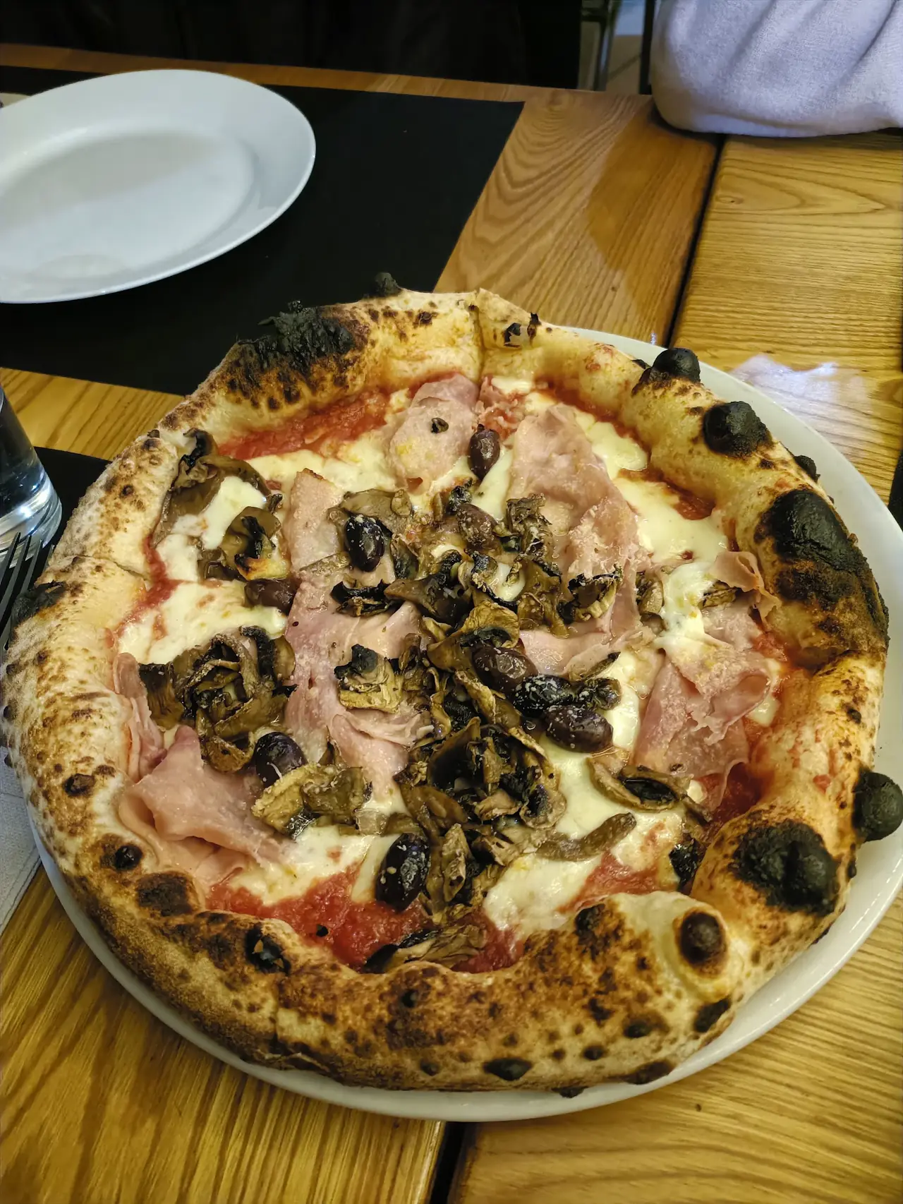 A pizza topped with ham, mushrooms, olives and artichokes