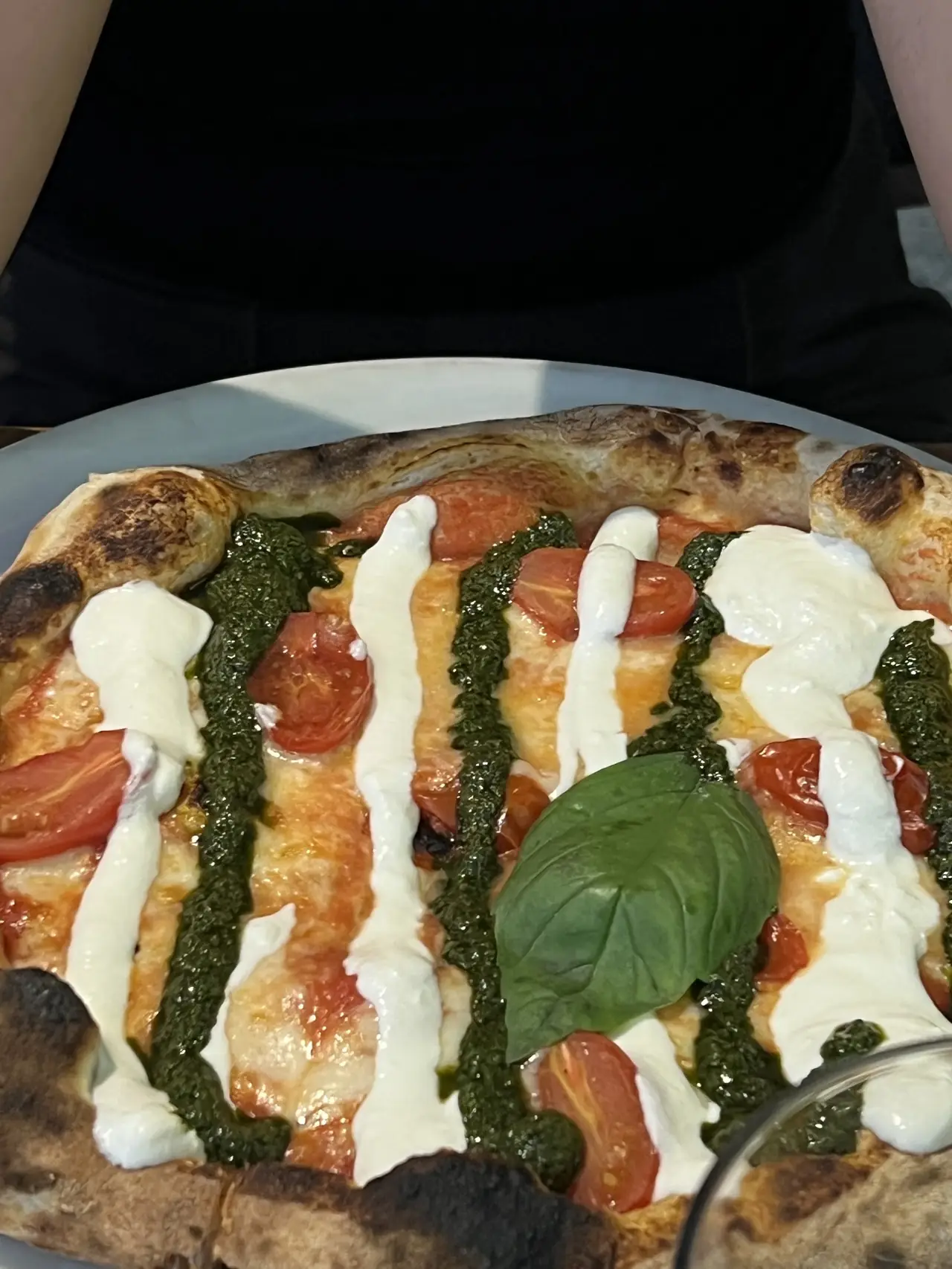 A pizza with tomato, pesto stripes, white cheese and a basil leaf