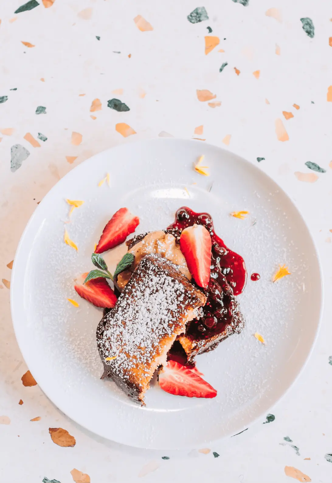 Powdered-sugar-dusted French toast with sliced strawberries and berry compote on a white plate at Picnic