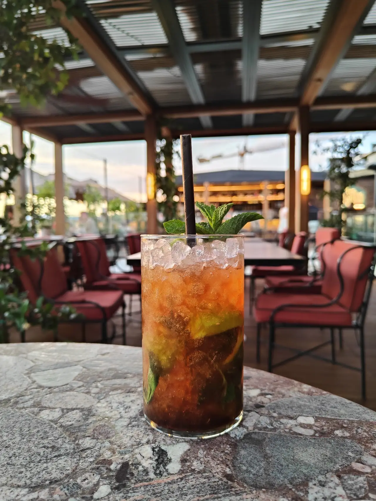 A tall cocktail with ice and a mint garnish on a stone table, rooftop terrace in the background.