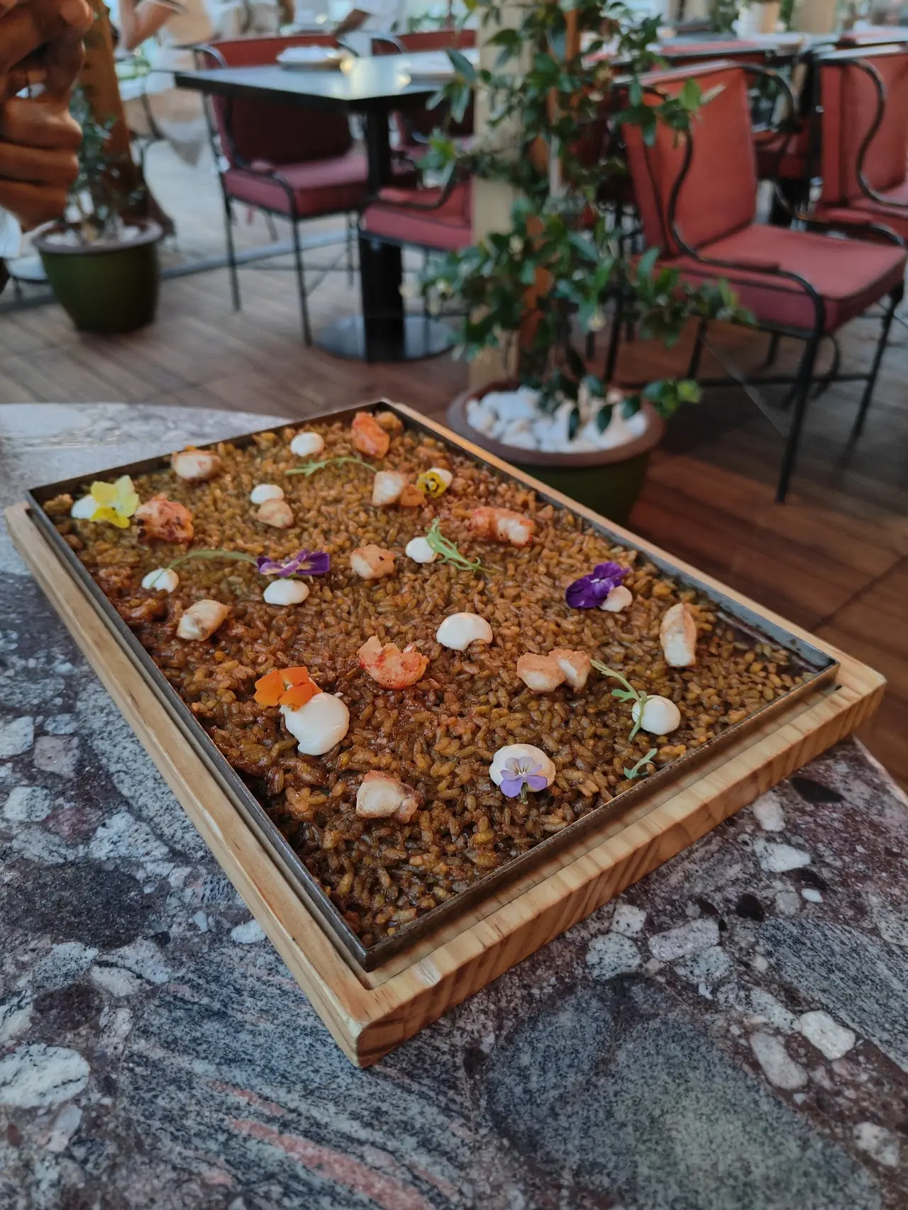 A wooden tray of small bites on a bed of grains, garnished with edible flowers.
