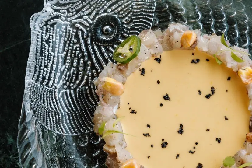 Ceviche-style dish with egg yolk sauce, black caviar, and jalapeño on a fish-patterned glass plate