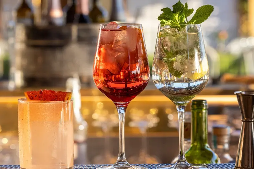 Three cocktails and a glass of wine lined up on a bar counter