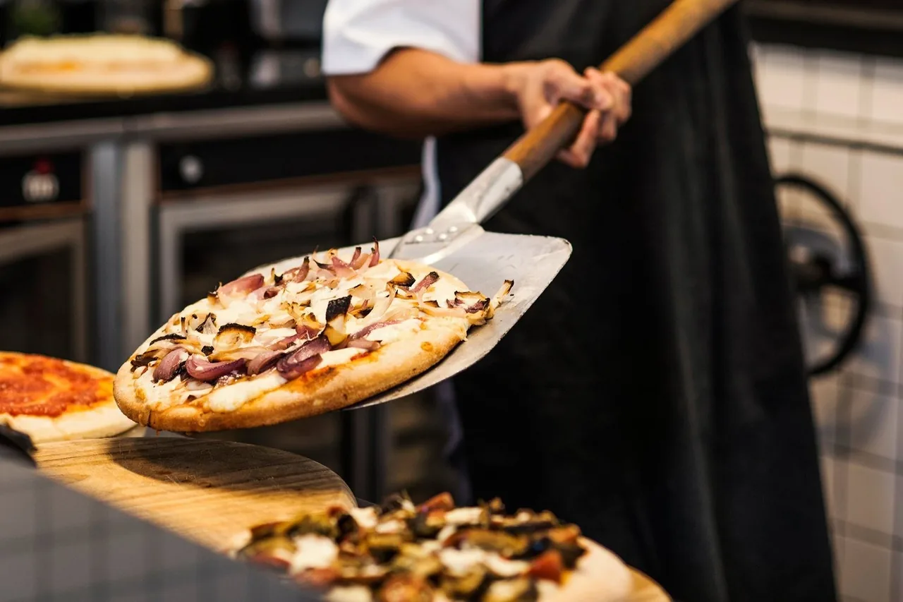 A cook lifting a onion-topped pizza on a peel