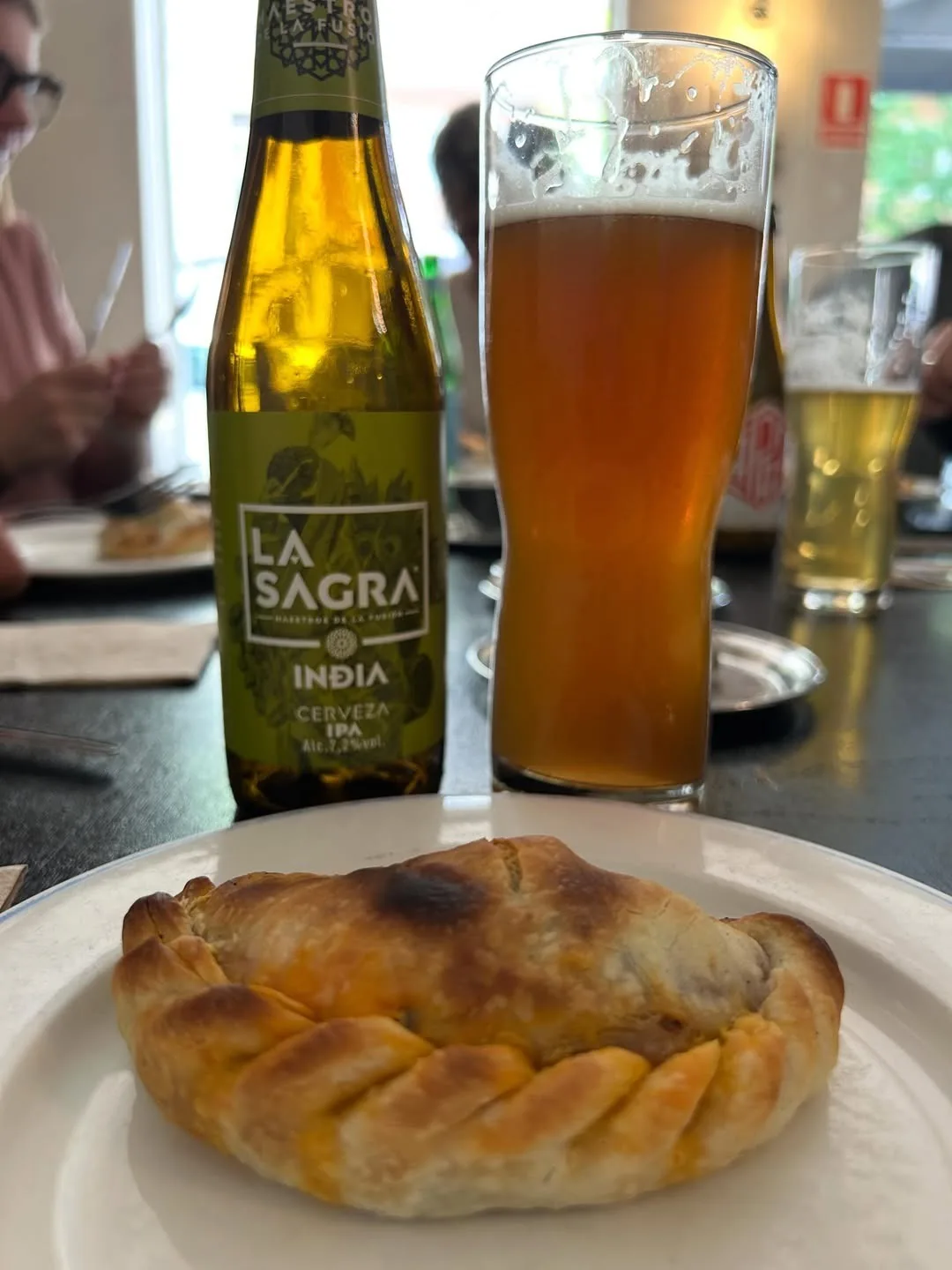 A golden braided calzone on a white plate next to a glass of beer and a bottle