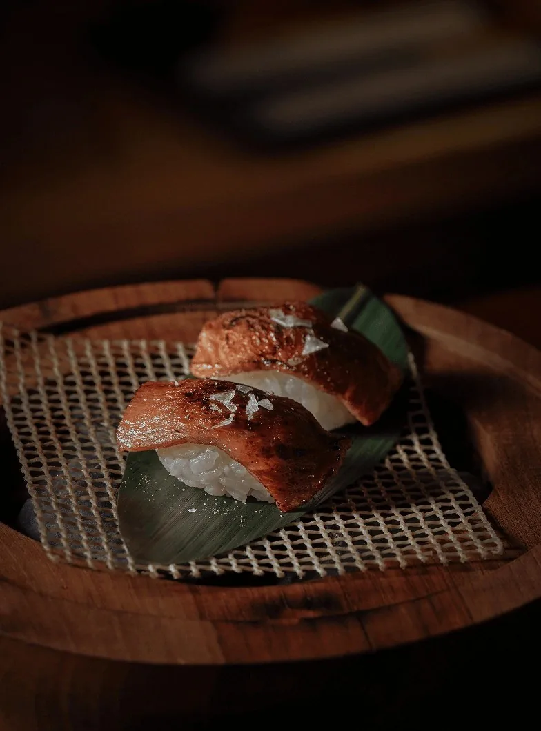 A piece of grilled nigiri on a leaf over a small grate